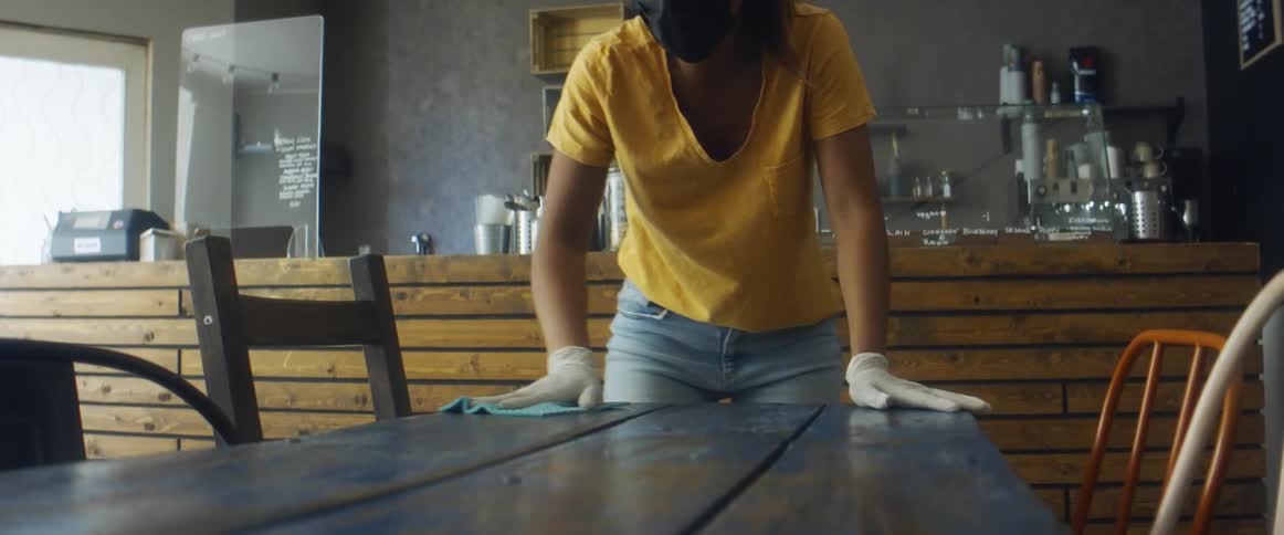 A woman cleans the surface of a table with a cloth in a cafe during the day