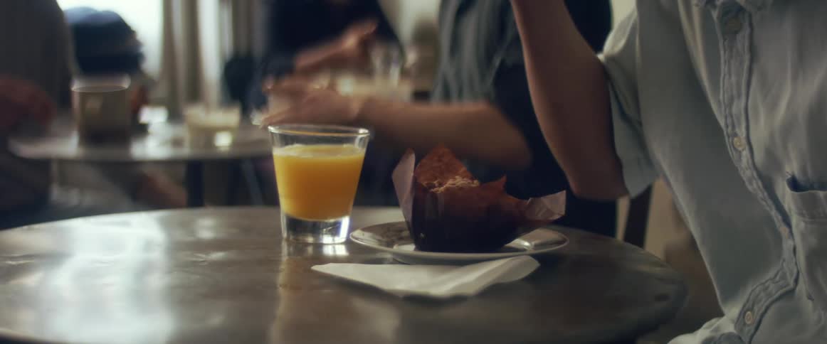 A customer eats a muffin at a small table in a cafe during the day