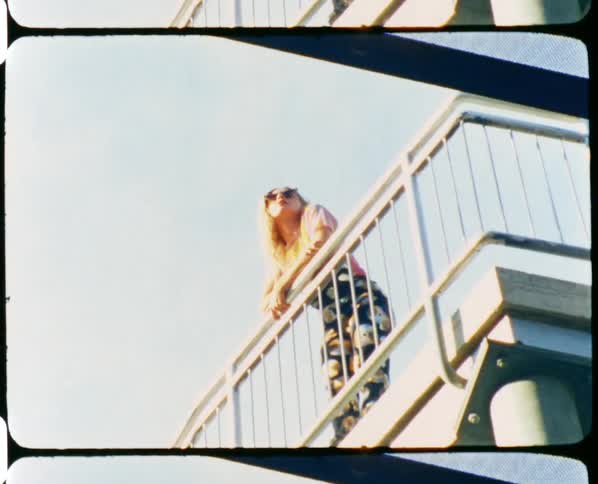 A woman with sunglasses standing next to a handrail but the sky and clouds above