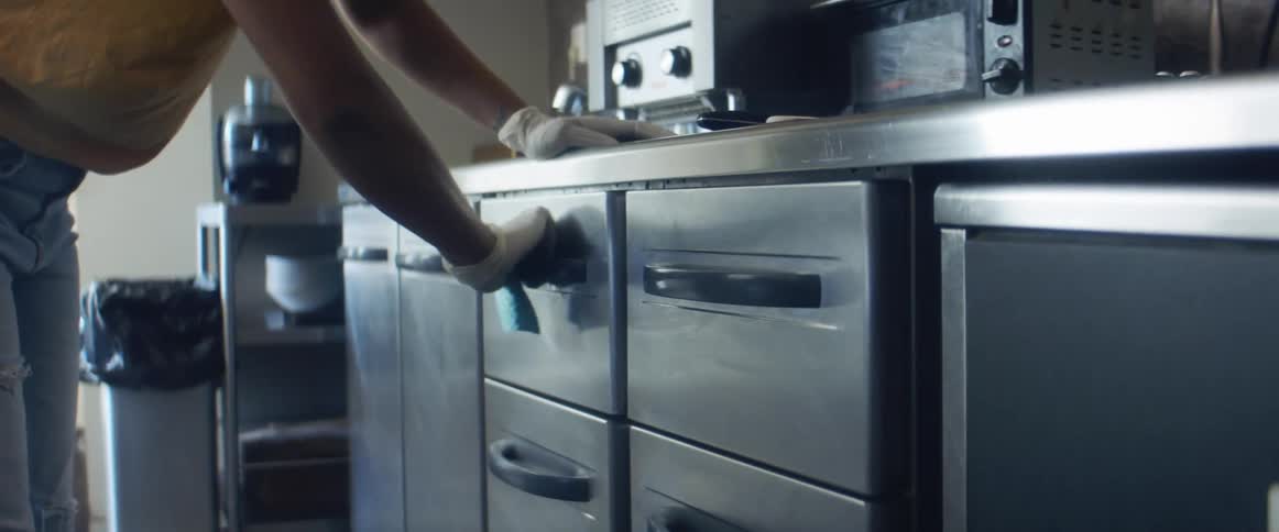 A woman in a room with gloves and a sponge cleaning the handle of drawers