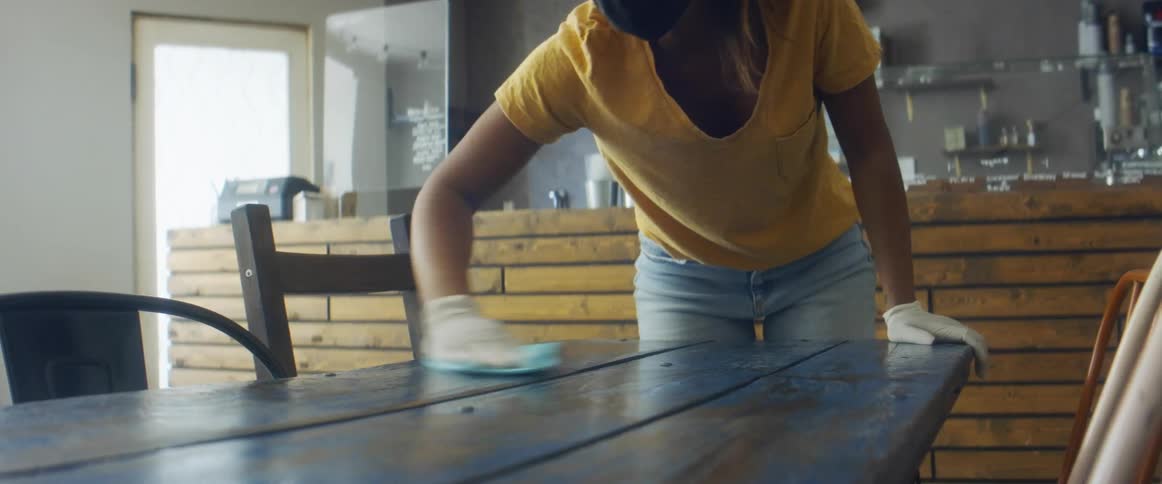A woman uses a cloth to wipe clean a table in an empty cafe