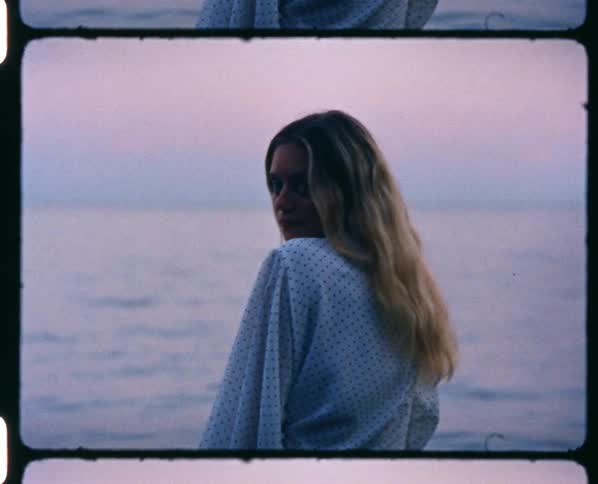 A woman wearing a long white robe is standing close to the waters edge