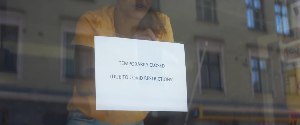 Woman posts sign regarding closing due to covid in window reflecting opposing building