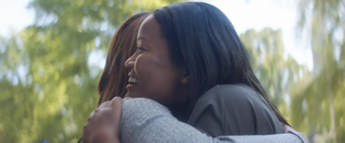 Two women smiling and hugging outside on a summer day
