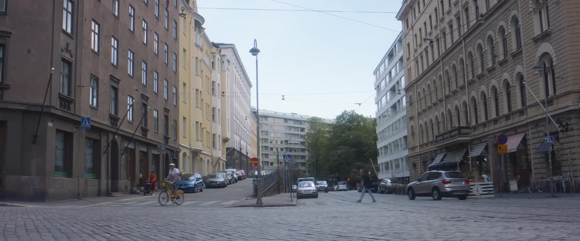 People sit at an outdoor cafe as cars and bikes travel on cobblestone streets