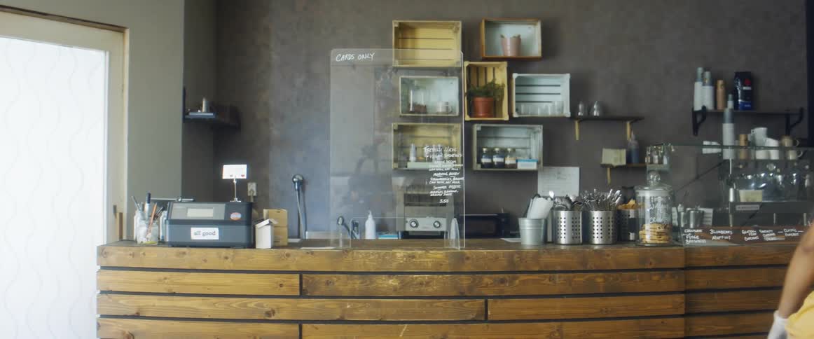 A woman in a coffee shop with gloves and a mask moving a glass display