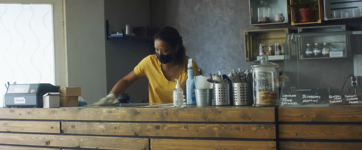 A woman uses a spray bottle to clean the counter in a cafe