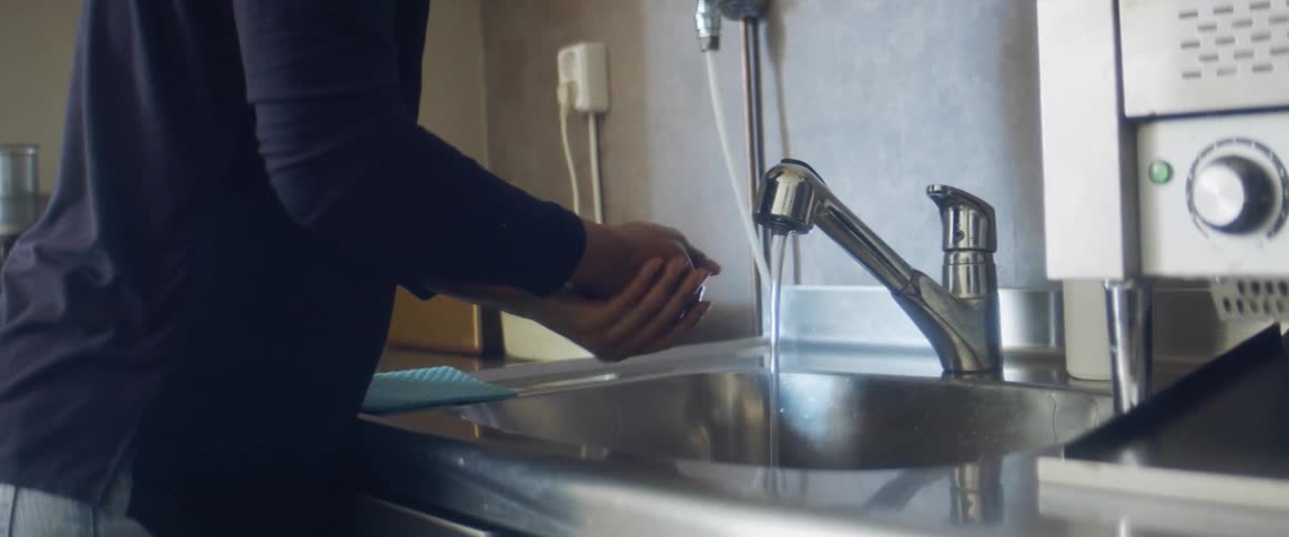 A person in a kitchen washing their hands in a sink with a faucet