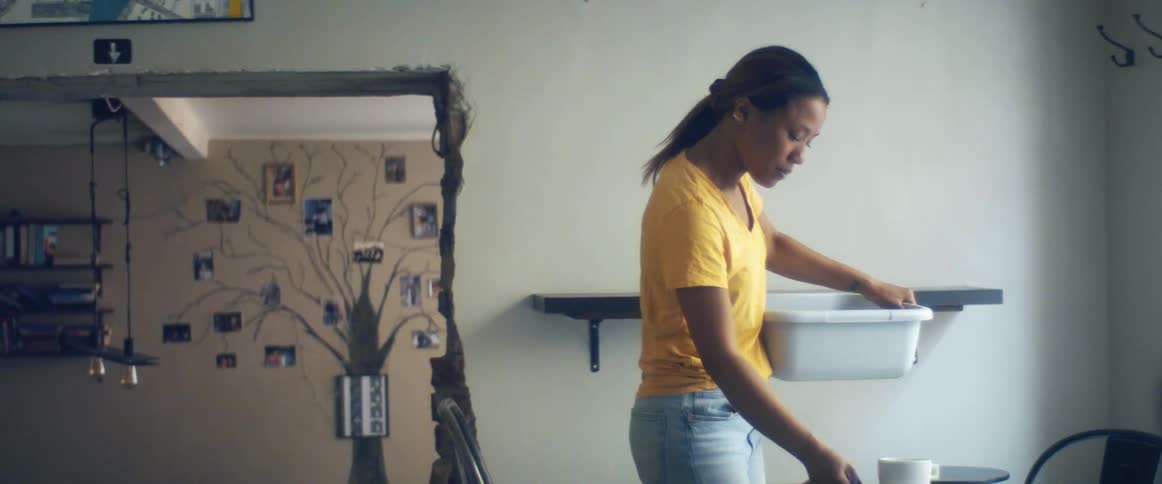 A woman in a room taking a cup and saucer from a table with a wall in the background