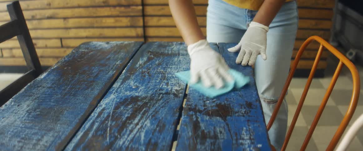 A woman wipes a dining table in a restaurant with a cloth
