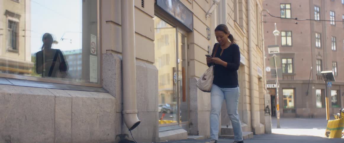 A woman takes a picture inside a store window with her phone and then walks down the street texting