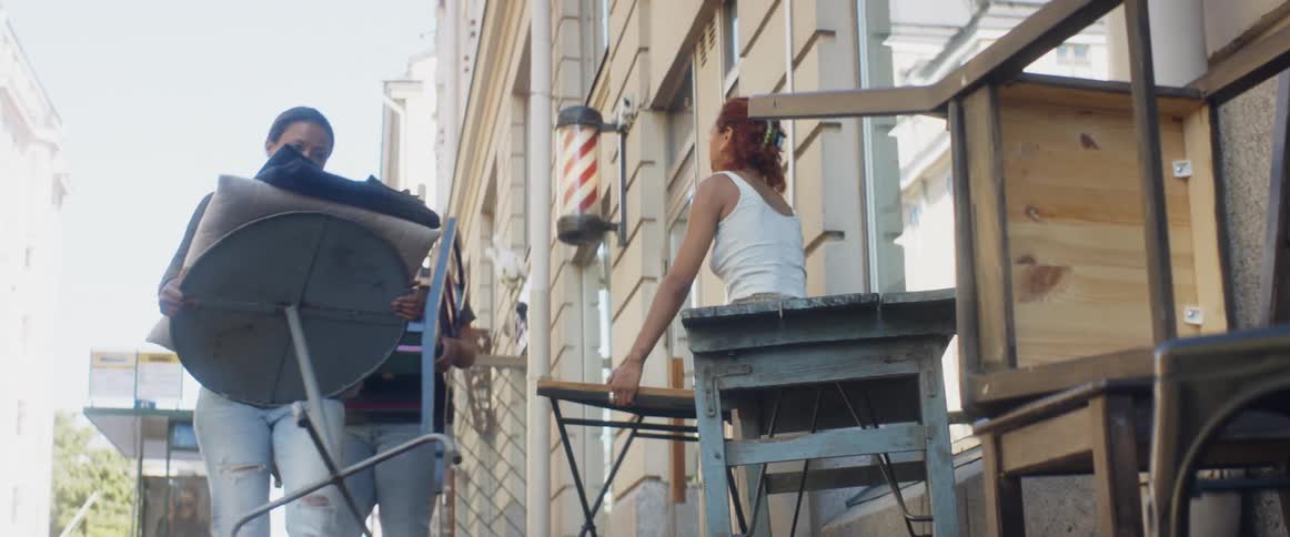 Three women next to a building on a city street moving tables and chairs
