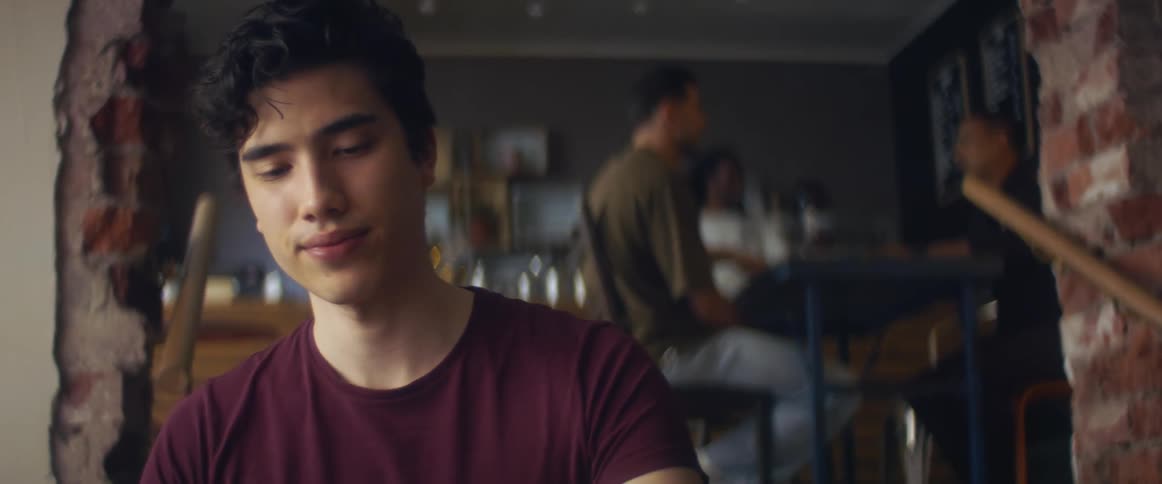 Man takes drink sitting in coffee shop as waitstaff moves around between table and front counter