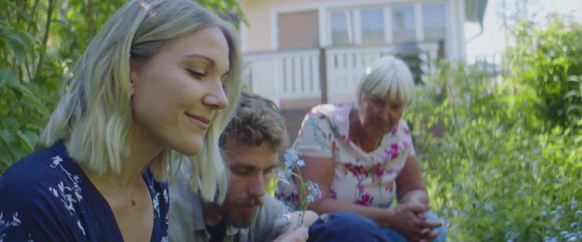 A woman smells a flower from the garden as her husband holds their child and grandma looks on