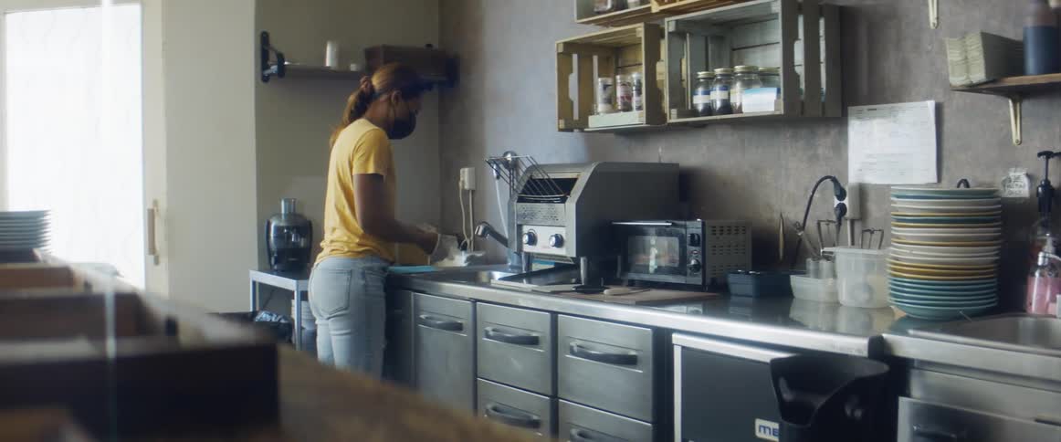 A female cafe employee puts on gloves standing at a sink