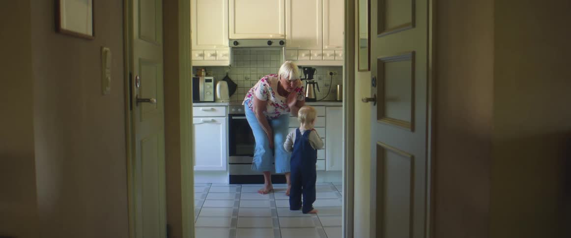 A woman leans down to talk to her grandson in the kitchen