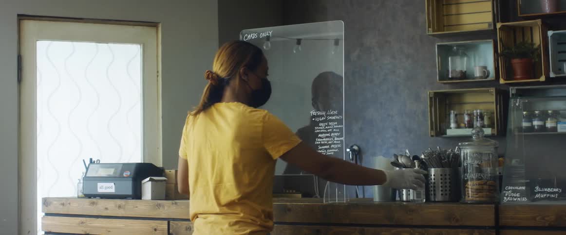 An employee in a cafe puts a plastic screen up on a counter and sets hand santizer in front of it