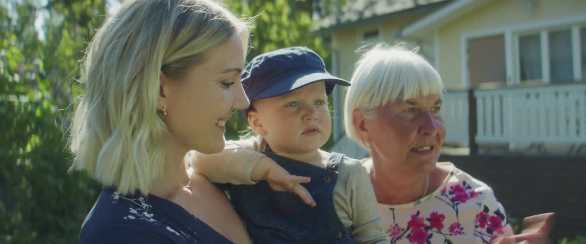 A woman holds her toddler son standing next to her own mother