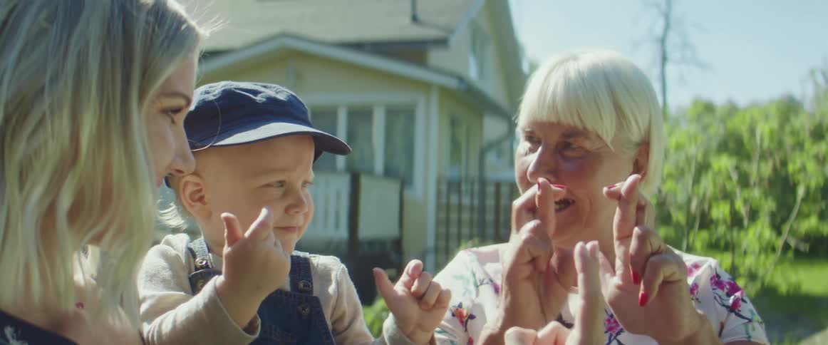 A woman holds a toddler boy beside the grandmother as they all do sign language