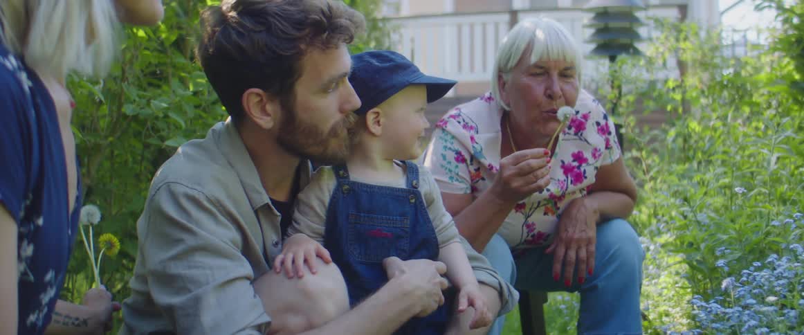 Grandmother and parents crouch in garden showing child how to dandelions