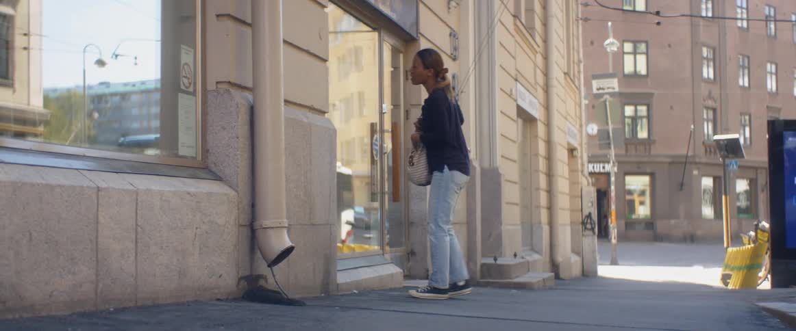 Young woman walking down the street stops in front of a shop to take a picture with her phone