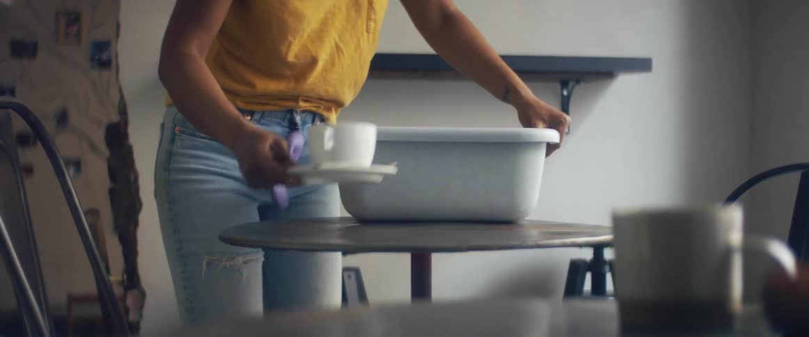 A woman in a room taking a cup and saucer from a table with a wall in the background