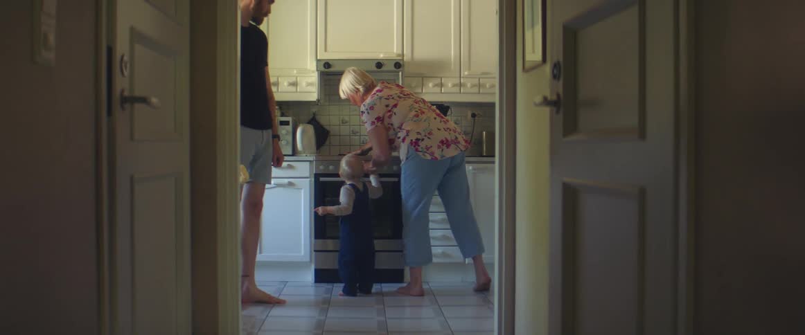 A man a woman and a child in a kitchen with the woman cleaning the stove