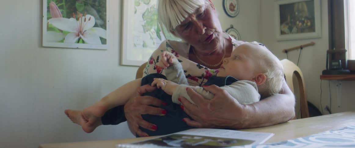 A grandmother holds a little boy and rocks him back and forth at the kitchen table