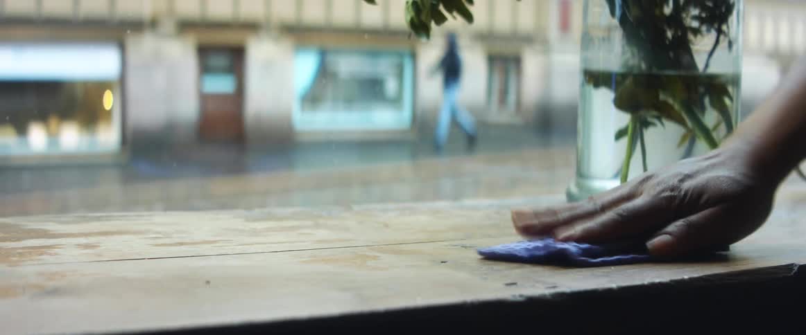 A restaurant employee clearing a plate of food and wiping a wood table