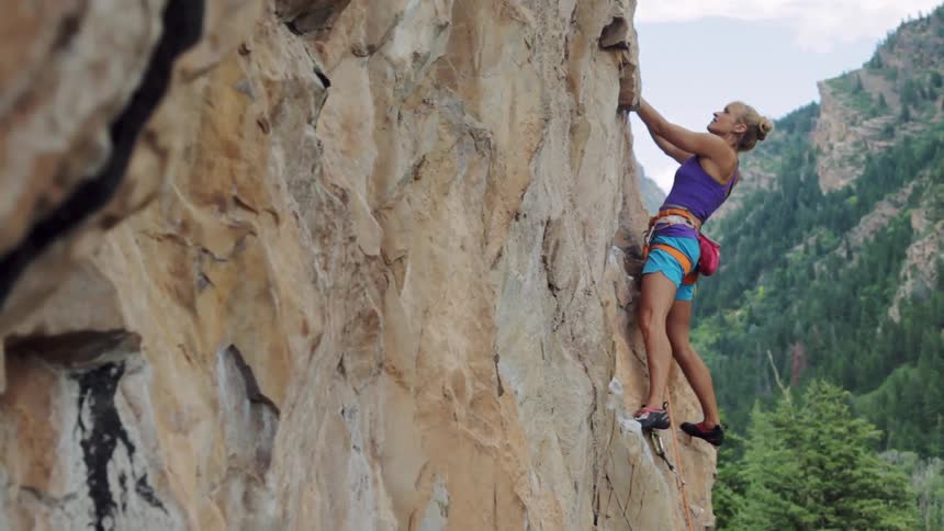 A woman is rock climbing on the side of a cliff