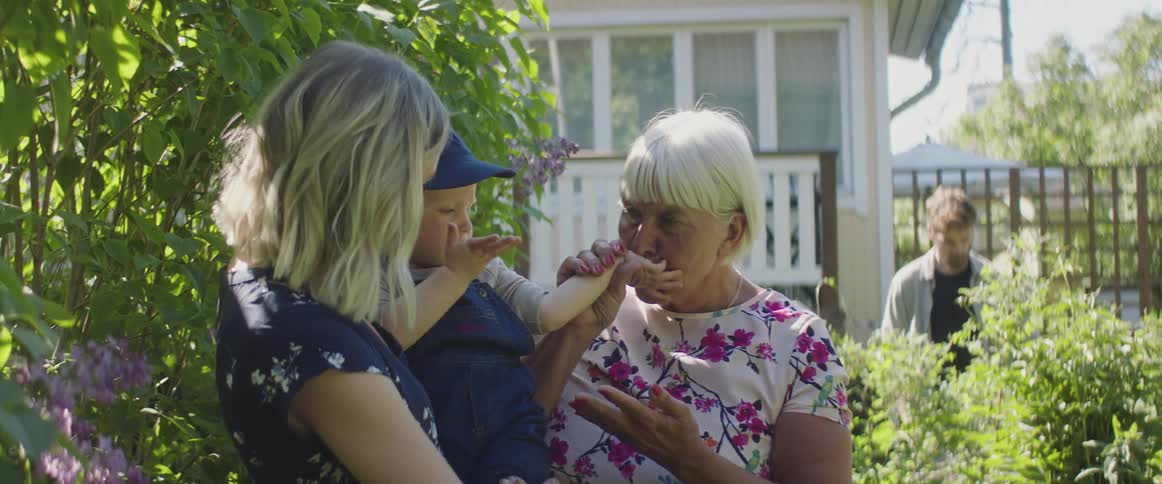 Grandma laughs and kisses baby while she and mom stand in the garden