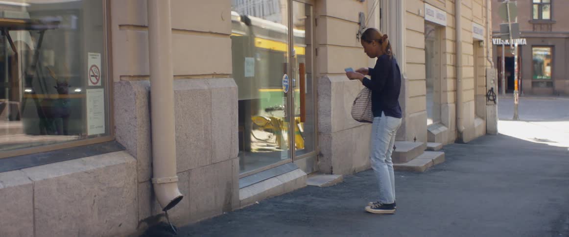 A woman with a bag walking on a city street and taking a picture with a smart phone
