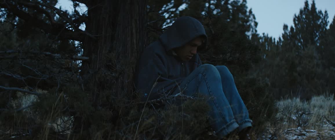A man shivers outdoors in a forest and looks sad