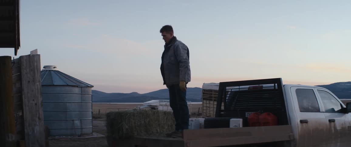 A man tosses a bale of hay from the bed of a pickup truck before climbing down