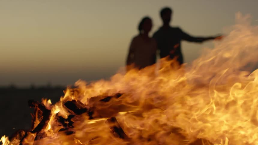 The silhouette of two people standing behind a burning flaming bonfire