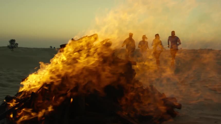 Four people are running in sand toward a fire