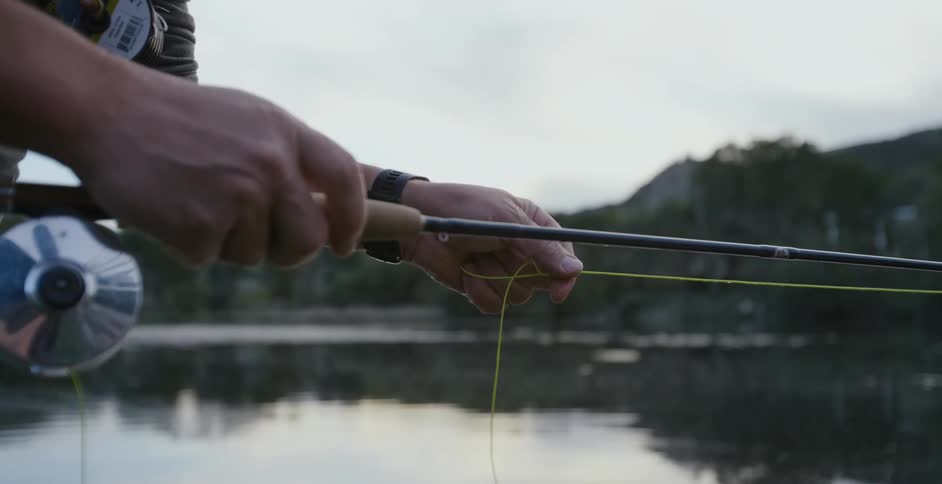 A person uses their fingers to pull on the fishing line of a fishing pole by a lake