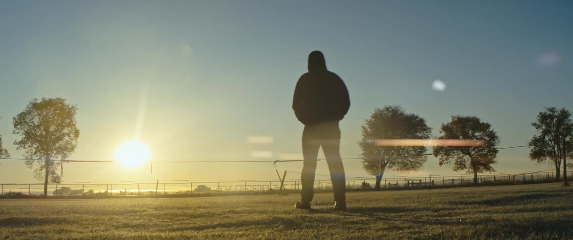 A silhouetted man walking across a field at sunset