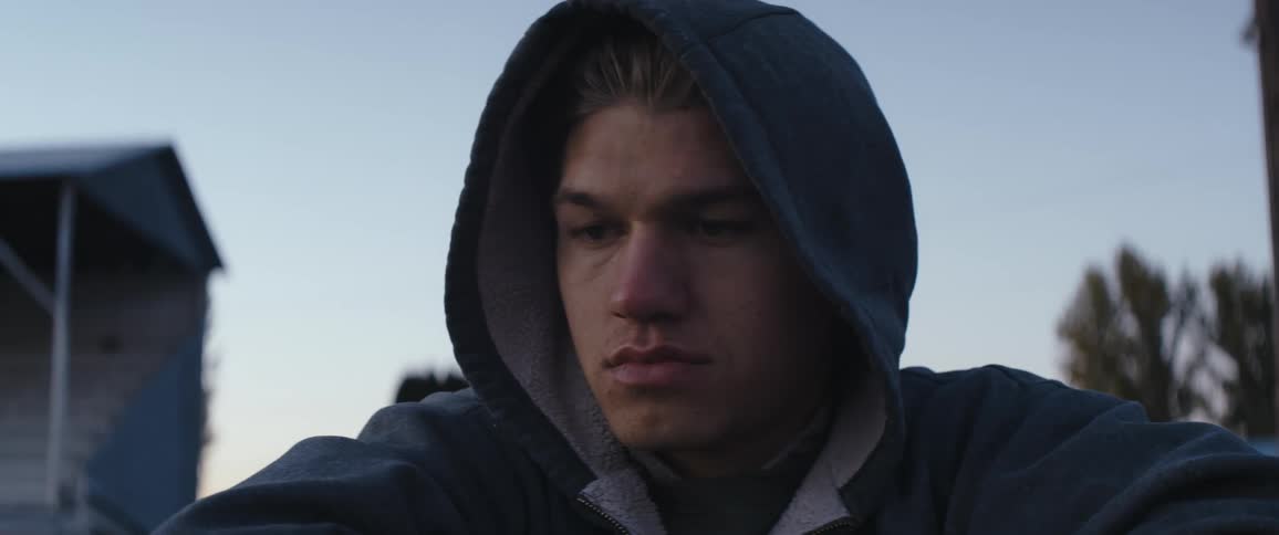 Young man wearing a hoodie sitting outdoors at evening