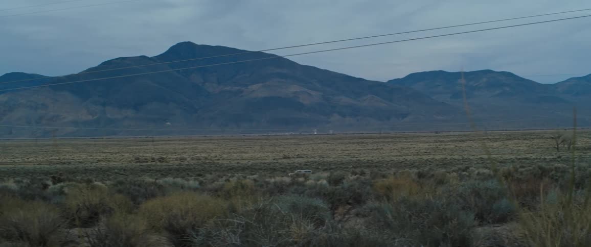 A 4x4 speeds on a dirt road lined with utility towers and mountains in the distance
