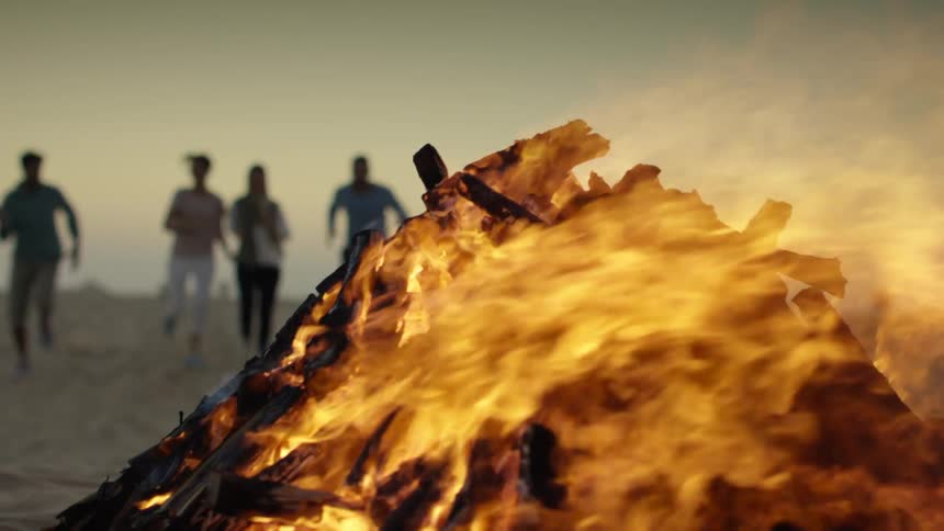 A group of friends run toward a burning bonfire on the beach