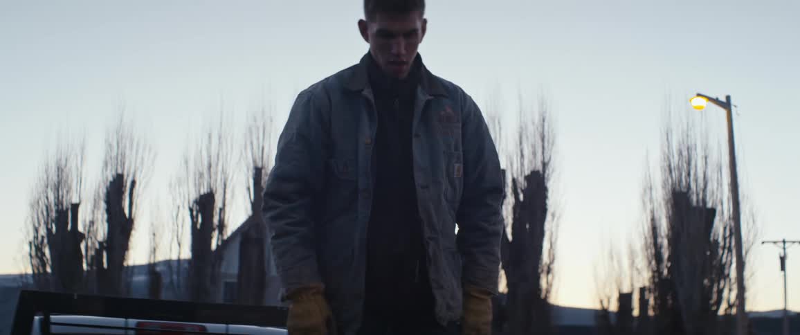 Young man unloading hay bales from the back of a truck at sunset