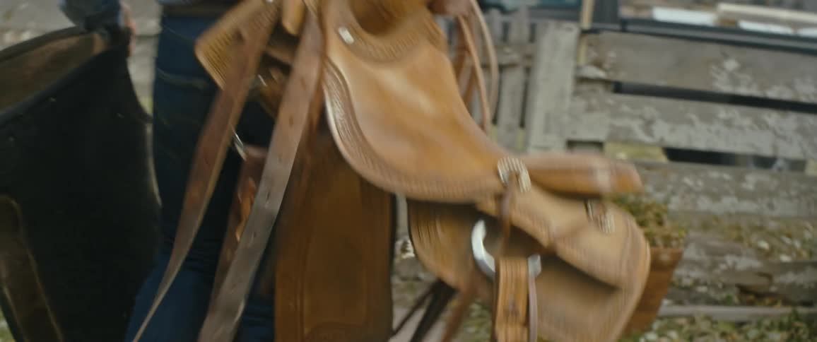 A man walks down a sidewalk carrying a saddle