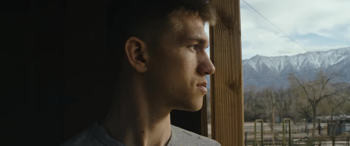 Young man looks out across a ranch with mountains in the background