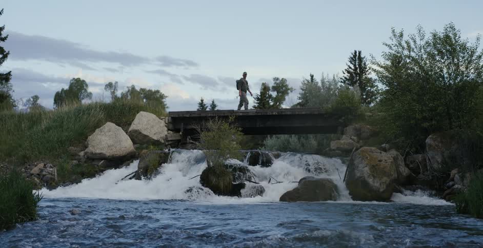 A person walking on a bridge over a river with the sky and clouds in the background