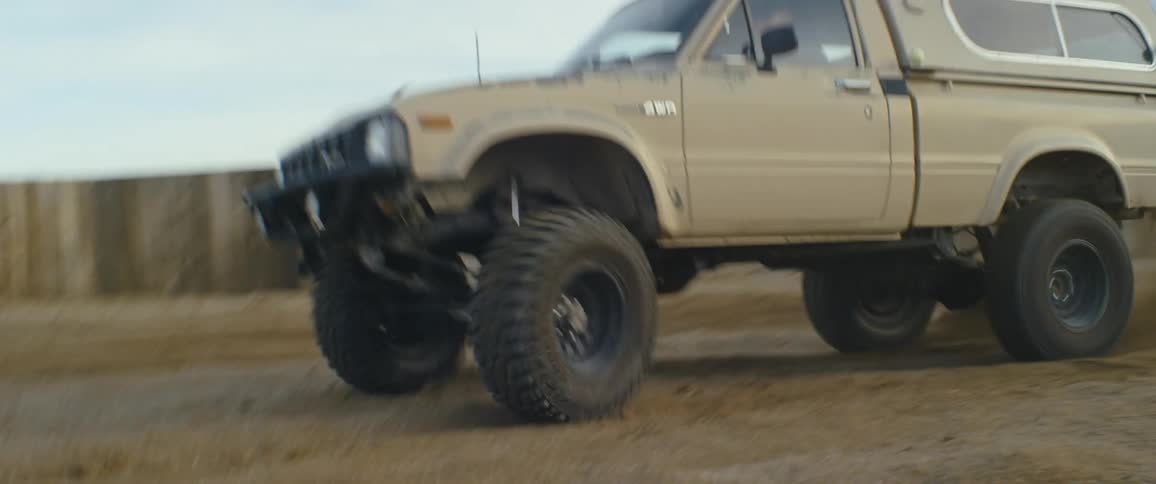 An old small pickup truck with a camper shell races around a dirt track