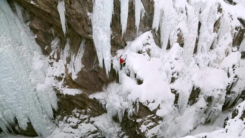 A person climbs up icy snowy rocks