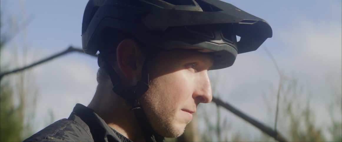 Man wearing bicycle helmet and standing outdoors raises his head