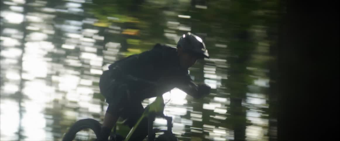 A man with a helmet riding a bicycle in the forest with the sky and clouds in the background
