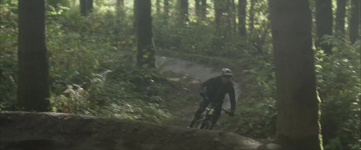 A man riding a mountain bike on a dirt trail in a forest and going over a jump